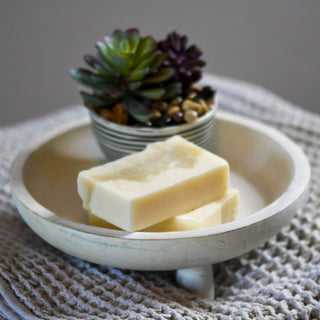 A raw bar of Simply Hypnotic Organic Soap with Geranium, Cedarwood & Patchouli Essential Oils, displayed in a white bowl with a knitted texture in the background.