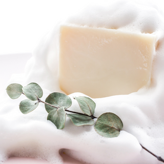 A raw bar of organic soap with basil, sage, and peppermint essential oils and leaves on top, surrounded by bubbles.